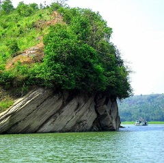 A scenic view of a rocky cliff covered with lush greenery, jutting out into a serene body of water with a boat sailing by.