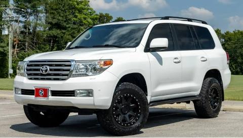 A white Toyota Land Cruiser SUV is parked in a lot with trees in the background.
