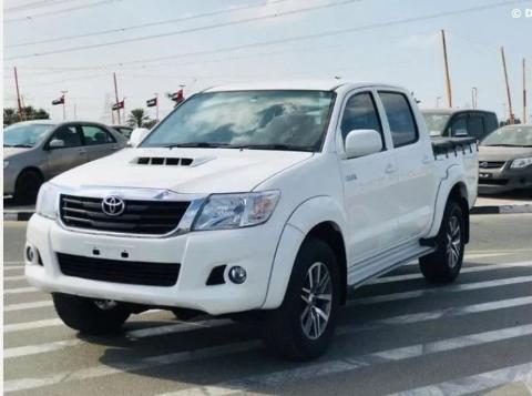 A white Toyota Hilux double cab pickup truck is parked on a zebra crossing in an outdoor setting with other cars in the background.