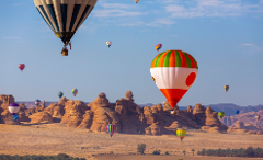 A picturesque desert landscape is dotted with unique rock formations and filled with a multitude of colorful hot air balloons floating under a clear blue sky.