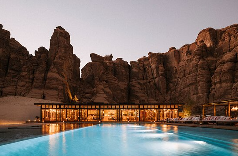 A building with a swimming pool sits in front of large rock formations at dusk.