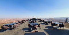 A scenic outdoor restaurant with tables and chairs overlooks a canyon landscape under a clear blue sky.