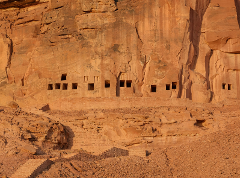 A cliff dwelling in a canyon wall with multiple openings and a staircase leading to it.