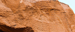 This image shows the Junagadh rock inscription of Rudradaman, an ancient carving on a reddish rock face featuring text written in an ancient script.