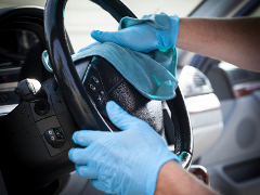 A person wearing blue gloves is cleaning a car steering wheel with a blue cloth.