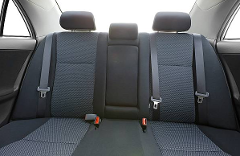 A car's back seat with three headrests, two seatbelts, and a center armrest.