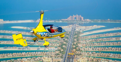 A yellow gyrocopter flies over Dubai's Palm Jumeirah, with the Atlantis hotel visible in the background.