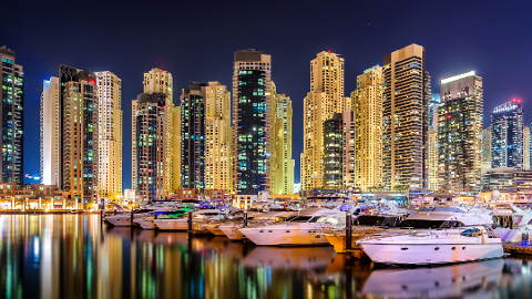 Night view of Dubai Marina with numerous skyscrapers illuminated against the dark sky and a line of white yachts docked in the foreground.