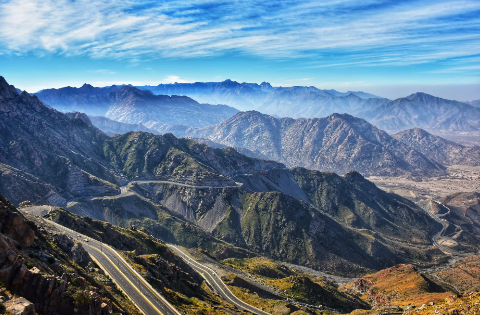 A stunning aerial view of winding roads cascading down a mountainous landscape under a blue sky.
