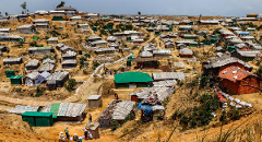 This aerial view depicts a densely packed refugee camp with makeshift shelters scattered across a hilly landscape, showcasing the challenging living conditions.