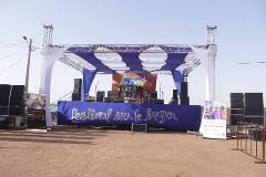 A stage is set up for the "Festival sur le Niger" with musical equipment, banners, and promotional posters against a clear sky.