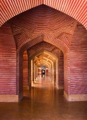 A long corridor is formed by repeating arches with striped red and white walls, converging to a blue-tiled doorway in the distance, creating a sense of depth and perspective.