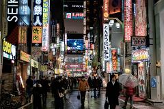 This photo captures a bustling street scene in Shinjuku, Japan, illuminated by vibrant neon signs and filled with pedestrians on a wet evening.