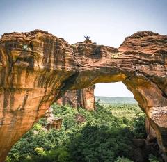 Full Day Tour To Siby And Bamako A person stands with arms outstretched on a massive rock arch overlooking a lush green forest.