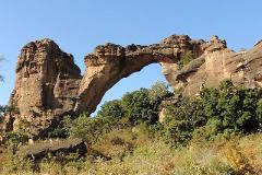 Full Day Tour To Siby And Bamako A dramatic natural rock arch spans across a valley, with rugged cliffs and lush green vegetation under a clear blue sky.