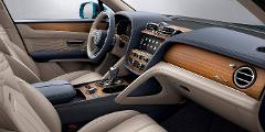 Interior of a Bentley Bentayga Azura featuring light beige seats, dark blue accents, and wood trim on the dashboard and doors.