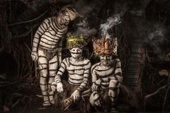 Three men in traditional attire and body paint pose in a Papua New Guinean forest setting.