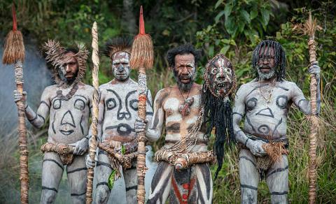 A group of four men with elaborate body paint and traditional accessories stand proudly against a lush green background, seemingly part of a cultural display or ceremony in Papua New Guinea.
