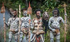 A group of four men with elaborate body paint and traditional accessories stand proudly against a lush green background, seemingly part of a cultural display or ceremony in Papua New Guinea.