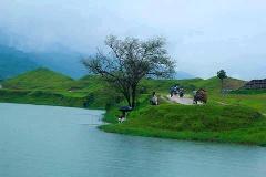 A serene landscape with rolling green hills, a lake, and people engaging in daily life, including fishing and transportation on a cloudy day.