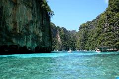 This image showcases a stunning tropical scene with turquoise waters, towering limestone cliffs covered in lush vegetation, and several boats dotting the water.