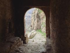 A stone archway frames a rugged, stone staircase leading to a mountainous landscape.