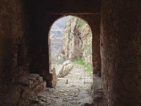 An arched stone doorway opens onto a weathered stone staircase ascending along a cliffside, framed by rugged stone walls.