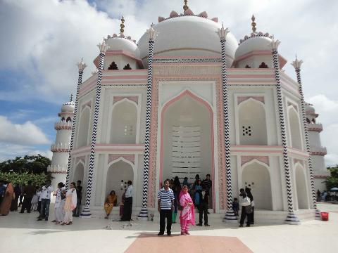 5-Day Dhaka Cultural Heritage Tour: Floating Markets & River Life Experience A white, domed building with pink and blue accents, resembling the Taj Mahal, stands under a cloudy sky as a crowd of people gathers in front of it.