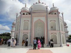5-Day Dhaka Cultural Heritage Tour: Floating Markets & River Life Experience A white, domed building with pink and blue accents, resembling the Taj Mahal, stands under a cloudy sky as a crowd of people gathers in front of it.