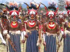 A group of indigenous men in Papua New Guinea wear traditional dress and face paint, holding spears and axes, at the Goroka Show festival.