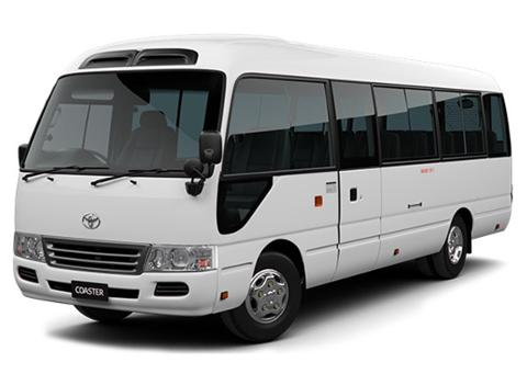 This is a white Toyota Coaster minibus, viewed from the front and side. It features tinted windows, a distinctive roof design, and the word "COASTER" displayed on the front.