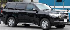 A sleek black Toyota Land Cruiser SUV is parked on a paved surface, exhibiting its prominent grill and rugged tires.