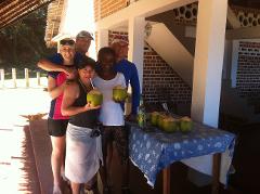 A group of five people stands posing with coconuts and a bottle on a table outside a building in Madagascar.