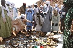 A group of people in traditional clothing gather around a display of various ingredients and goods on a white surface.