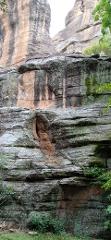 A rocky landscape featuring layered stone formations with some moss and vegetation clinging to the surfaces.