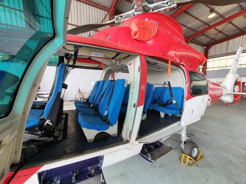 A red and white helicopter with its doors open, showing rows of blue seats inside, is parked in a hangar.