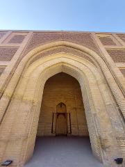 A low-angle shot of a large, ornate, light-yellow brick building with a grand arched entrance, showcasing detailed geometric patterns and an inner door.