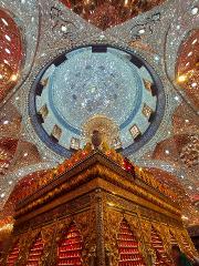 A low-angle shot captures a dazzling, ornately decorated mausoleum with a shimmering, mirror-tiled dome overhead.
