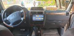 The image shows the dashboard and steering wheel of a Toyota Land Cruiser, with an aftermarket infotainment system installed in the center console.
