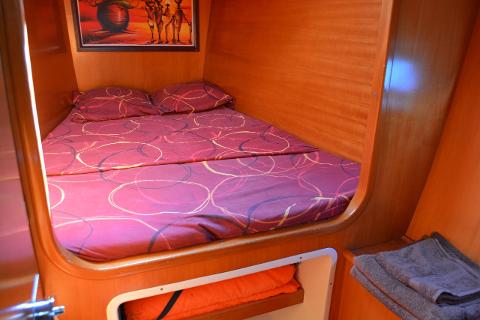 A cozy cabin bed with red patterned bedding sits within a wooden-paneled enclosure, accented by a framed artwork and storage shelves below.