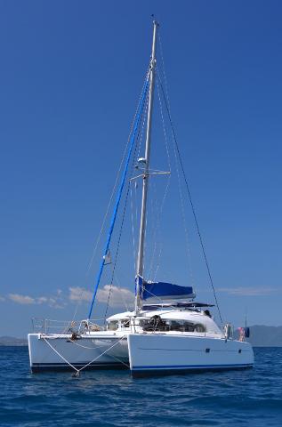 A white catamaran sailboat with a tall mast is floating on blue water under a clear blue sky.