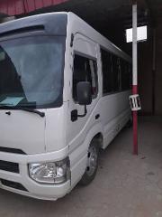 A white minibus is parked indoors next to a red and white pole, possibly in a garage or storage area.