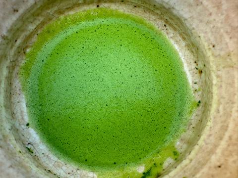 A close-up, overhead shot of a bowl of vibrant green matcha, with a foamy texture, contained within a crackled and aged ceramic cup.