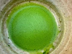 A close-up, overhead shot of a bowl of vibrant green matcha, with a foamy texture, contained within a crackled and aged ceramic cup.