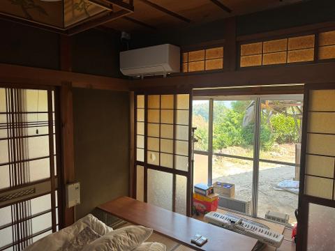 A scenic view of traditional Japanese houses with tiled roofs and lush green trees, set against a backdrop of rolling hills and a clear blue sky.