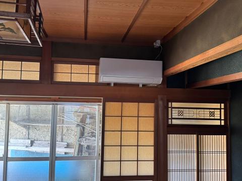 An indoor shot showing a room with traditional Japanese design, including sliding doors and windows with paper screens, wooden beams, and a modern air conditioning unit.