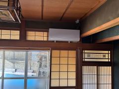 An indoor shot showing a room with traditional Japanese design, including sliding doors and windows with paper screens, wooden beams, and a modern air conditioning unit.