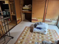 A Japanese room with futons and blankets stacked on a patchwork rug, with sliding doors and a closet filled with bedding.