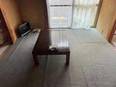 A room with a low table, a TV, a window with curtains, and carpeting.