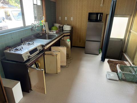 A cramped kitchen with open cabinet doors, a stove, sink, refrigerator, and a door leading to a bathroom.